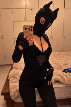 Mulher usando máscara de demônio com chifres, macacão preto e luvas de couro