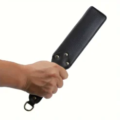 Paddle de spanking segurado na mão, mostrando o tamanho real e a alça com argola